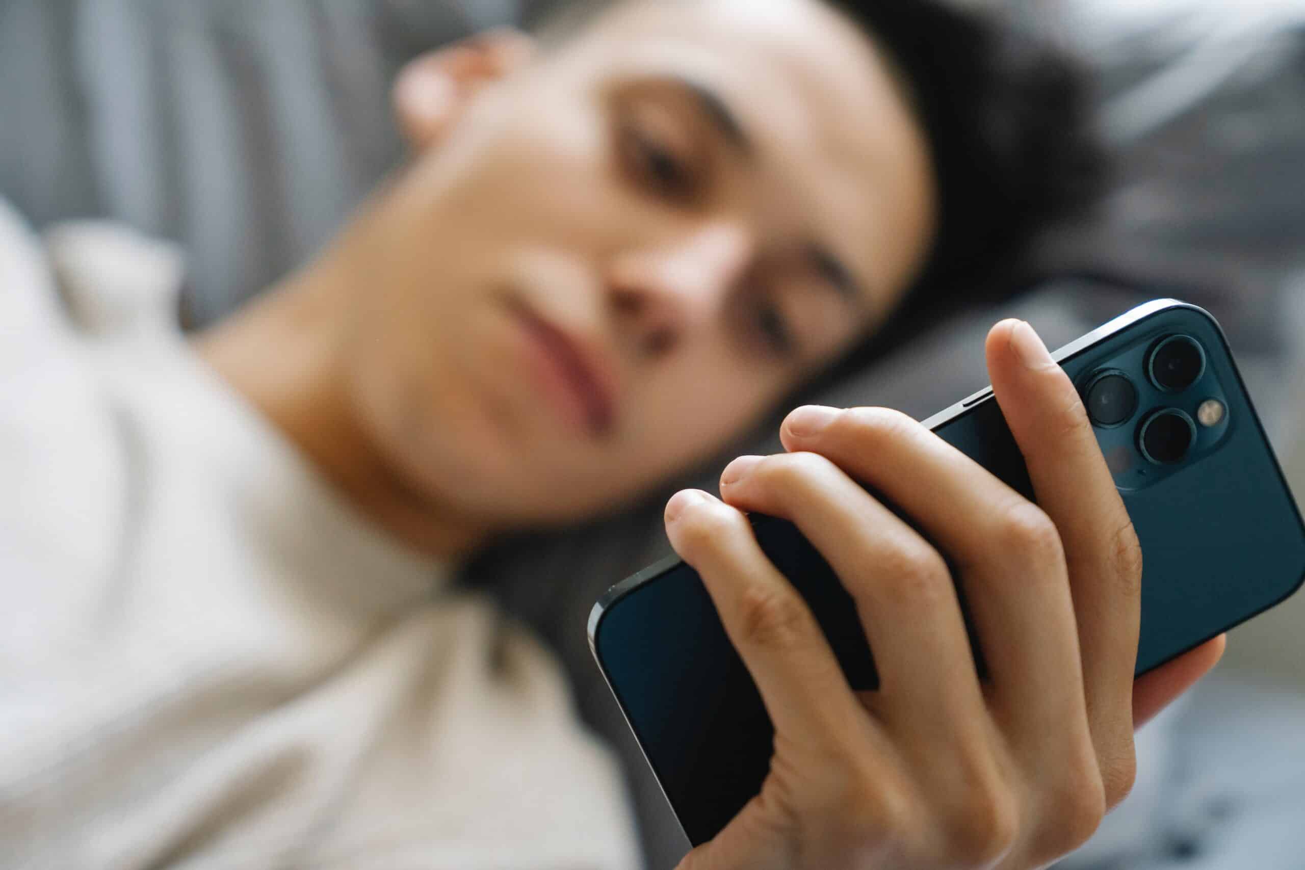Een jongen die net wakker is, zit op zijn telefoon, wat een teken kan zijn van een telefoonverslaving en een negatieve invloed kan hebben op zijn concentratie gedurende de dag.